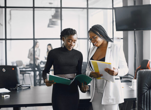 Business women talking near the desk during a coffee break in the hallway of the big corporation
