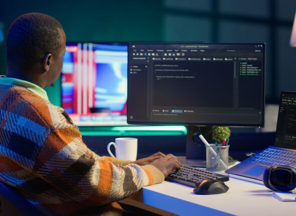 Programmer in home office concentrating on finding bugs while he codes on his computer. African american IT admin frowning while looking at screen, confused by errors in lines of code. Camera A.